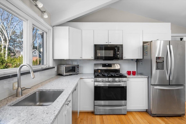 kitchen with a sink, stainless steel appliances, vaulted ceiling, white cabinetry, and backsplash