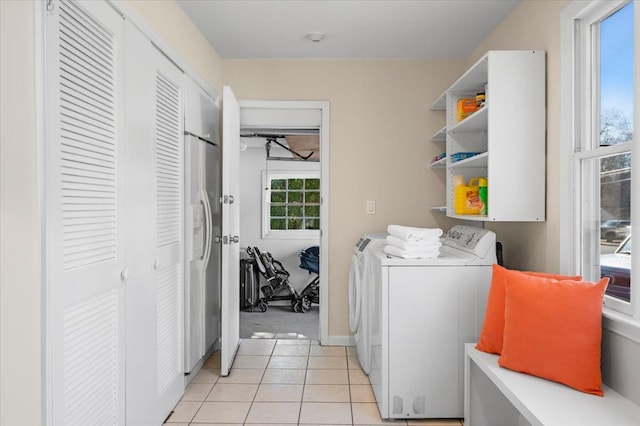 clothes washing area featuring light tile patterned floors, baseboards, washing machine and dryer, and laundry area