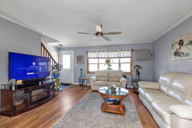 living area featuring ceiling fan, wood finished floors, baseboards, stairs, and crown molding