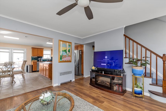 living area with stairway, radiator heating unit, light wood-style floors, ornamental molding, and baseboards