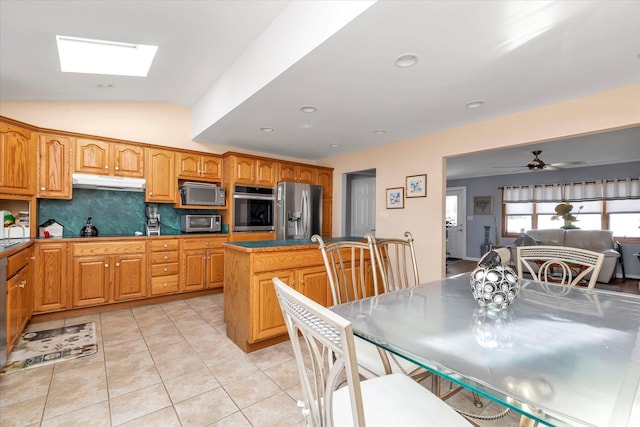 kitchen with light tile patterned flooring, under cabinet range hood, open floor plan, black appliances, and lofted ceiling with skylight