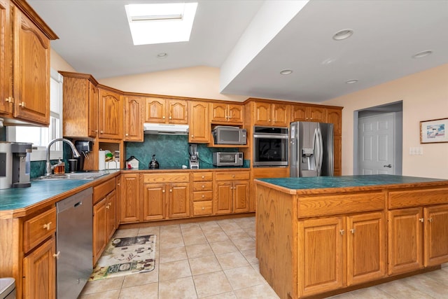 kitchen featuring stainless steel appliances, dark countertops, brown cabinets, and under cabinet range hood