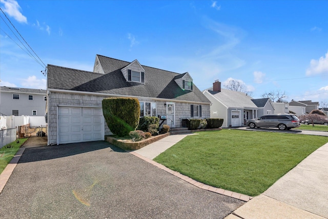 new england style home featuring a garage, driveway, roof with shingles, fence, and a front yard