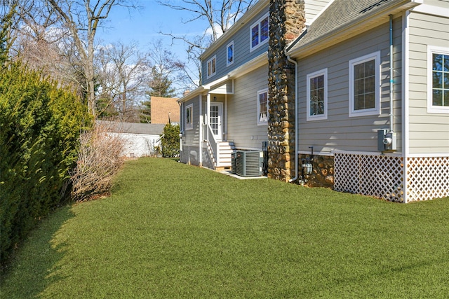 back of property featuring a yard, roof with shingles, central AC unit, and entry steps