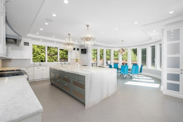 kitchen with a tray ceiling, a large island, hanging light fixtures, white cabinets, and light stone countertops