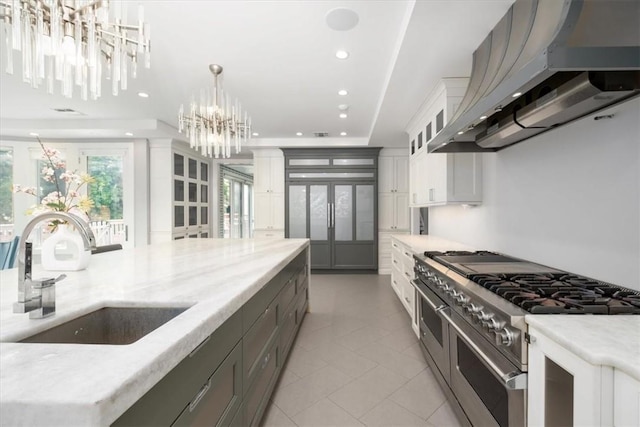 kitchen featuring hanging light fixtures, white cabinets, a sink, wall chimney range hood, and double oven range