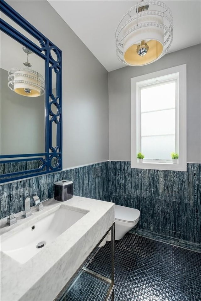 bathroom featuring tile patterned flooring, toilet, a wainscoted wall, a sink, and tile walls