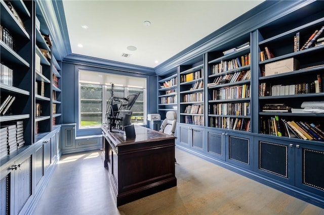 home office featuring built in features, visible vents, ornamental molding, wall of books, and wood finished floors