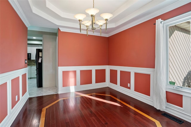 empty room with visible vents, a raised ceiling, hardwood / wood-style floors, and a chandelier