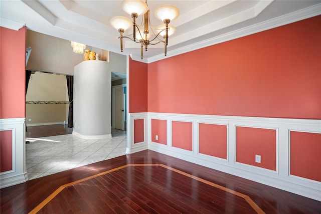 spare room with a chandelier, hardwood / wood-style floors, wainscoting, and a raised ceiling