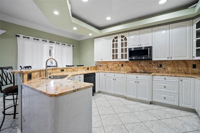 kitchen featuring a raised ceiling, stainless steel microwave, a sink, a peninsula, and a kitchen bar