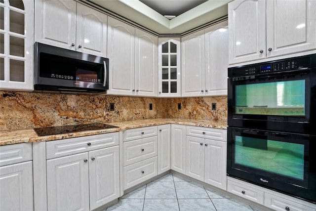 kitchen featuring white cabinetry, backsplash, light stone countertops, black appliances, and glass insert cabinets