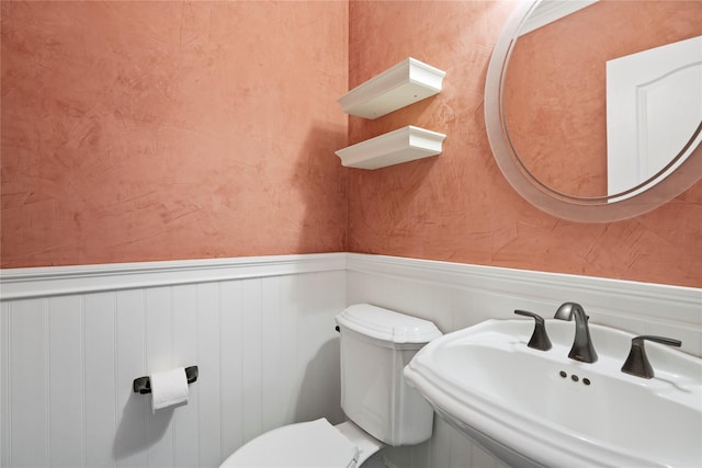 half bathroom with wainscoting, a sink, and toilet