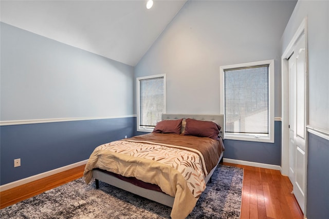 bedroom featuring high vaulted ceiling, a closet, baseboards, and hardwood / wood-style floors