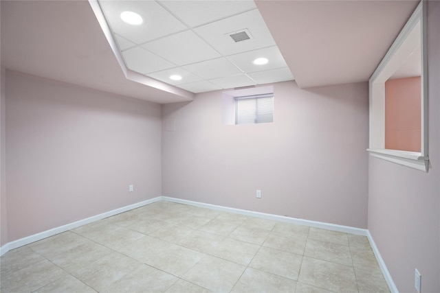 below grade area featuring light tile patterned flooring, a drop ceiling, recessed lighting, visible vents, and baseboards