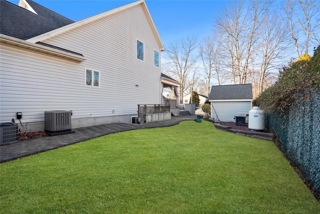 back of house featuring central air condition unit, a yard, roof with shingles, and an outbuilding