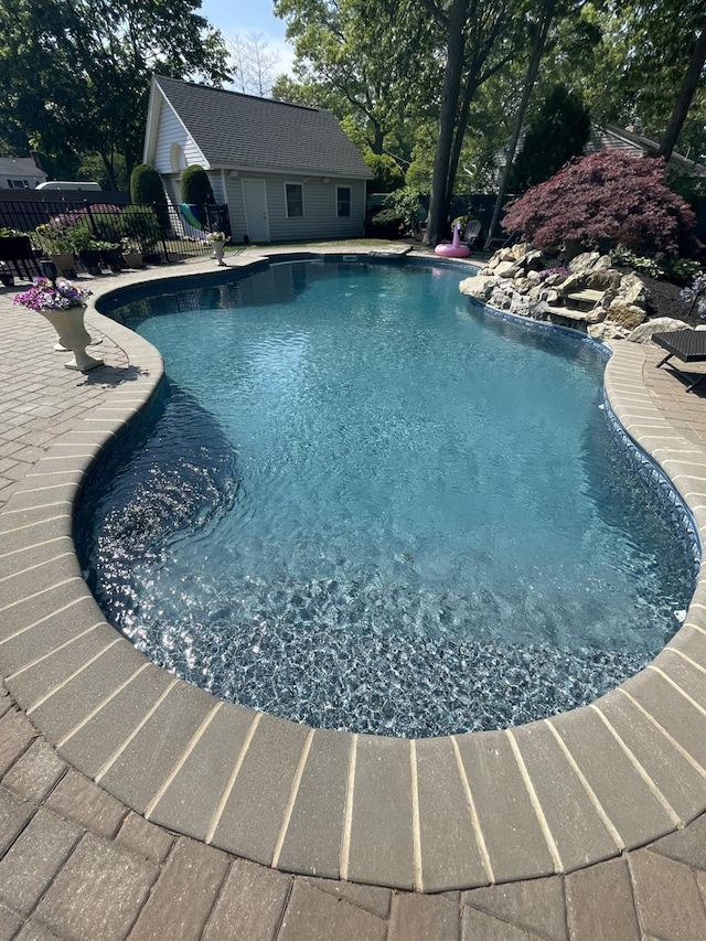 outdoor pool featuring an outbuilding, a patio, and fence