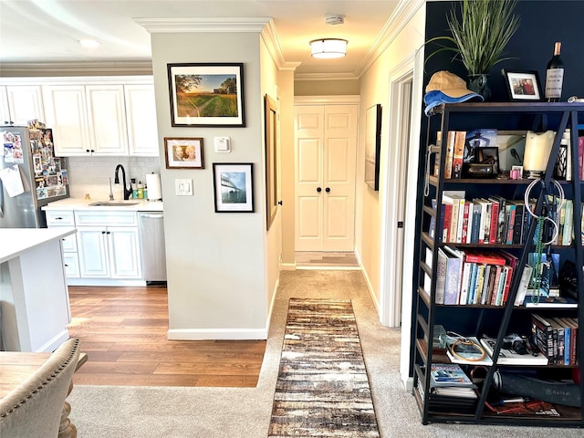 hallway featuring crown molding, light wood-style floors, a sink, and baseboards