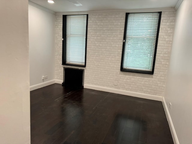 spare room featuring brick wall, baseboards, and wood finished floors