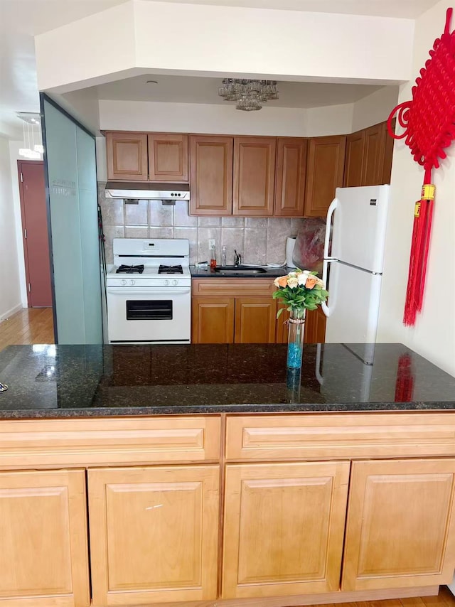 kitchen featuring white appliances, dark stone countertops, a sink, and tasteful backsplash