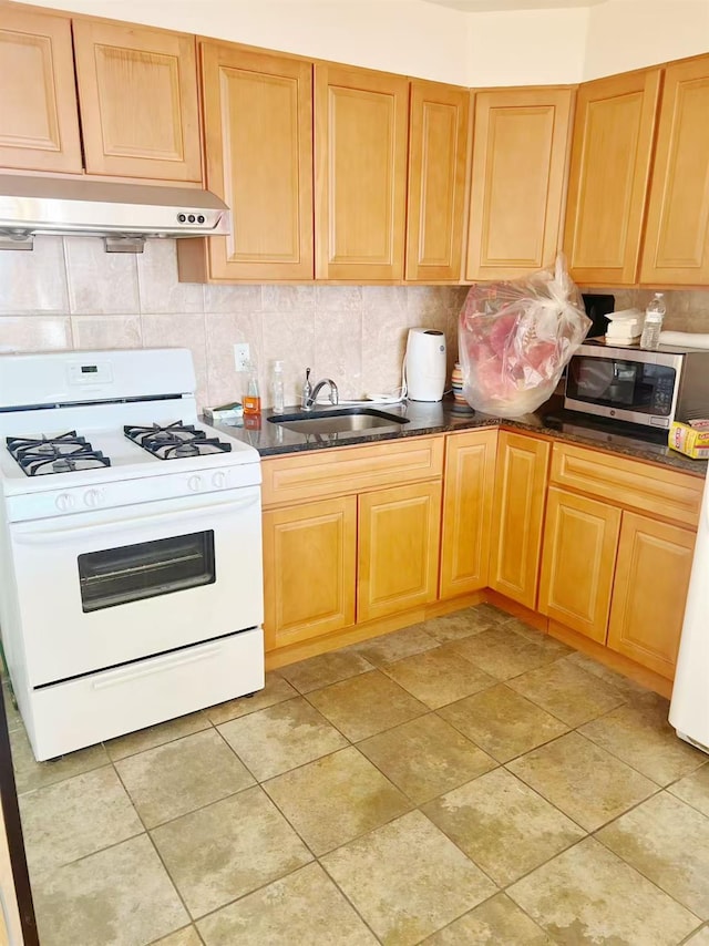 kitchen with white gas stove, dark countertops, stainless steel microwave, a sink, and under cabinet range hood