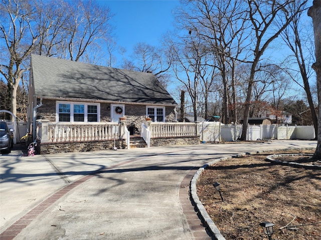 view of front of property featuring a shingled roof, concrete driveway, and fence