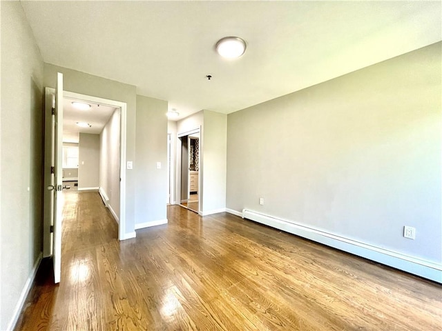 spare room featuring dark wood-style flooring, baseboard heating, and baseboards