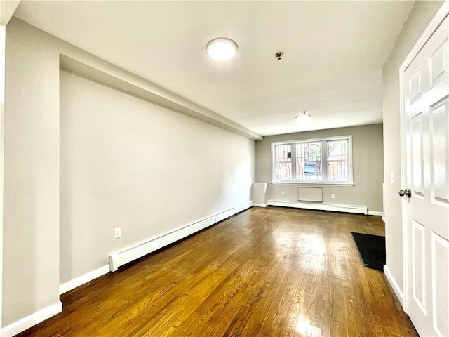 empty room with a baseboard radiator, baseboards, baseboard heating, and wood finished floors