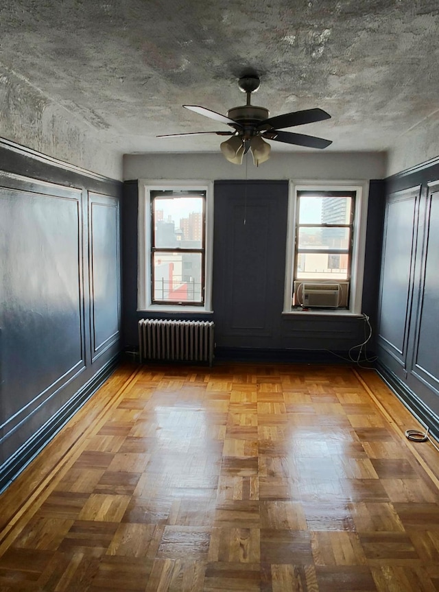 spare room with a textured ceiling, ceiling fan, radiator heating unit, and cooling unit