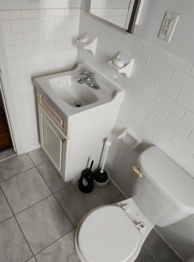 half bathroom with toilet, tile walls, vanity, and tile patterned floors