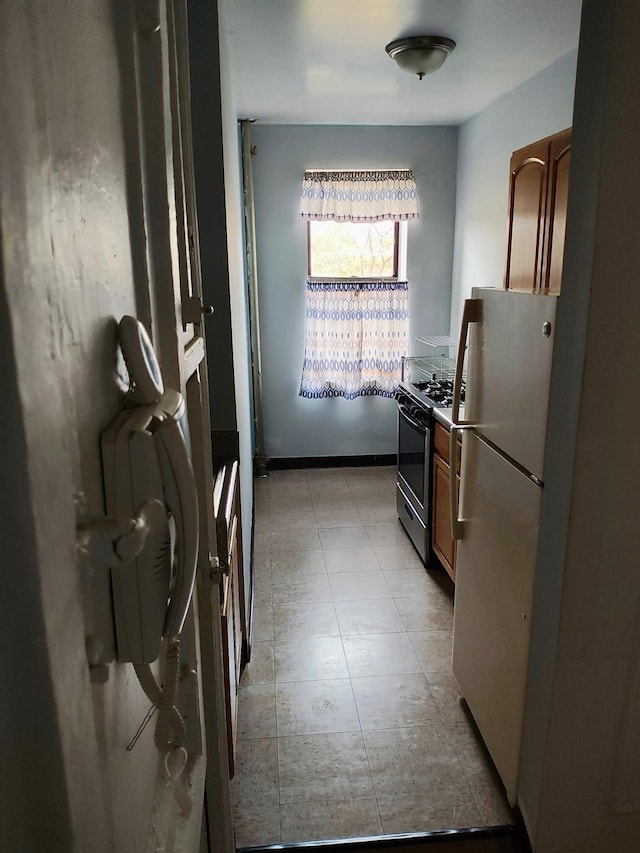 kitchen featuring brown cabinetry, freestanding refrigerator, and gas range