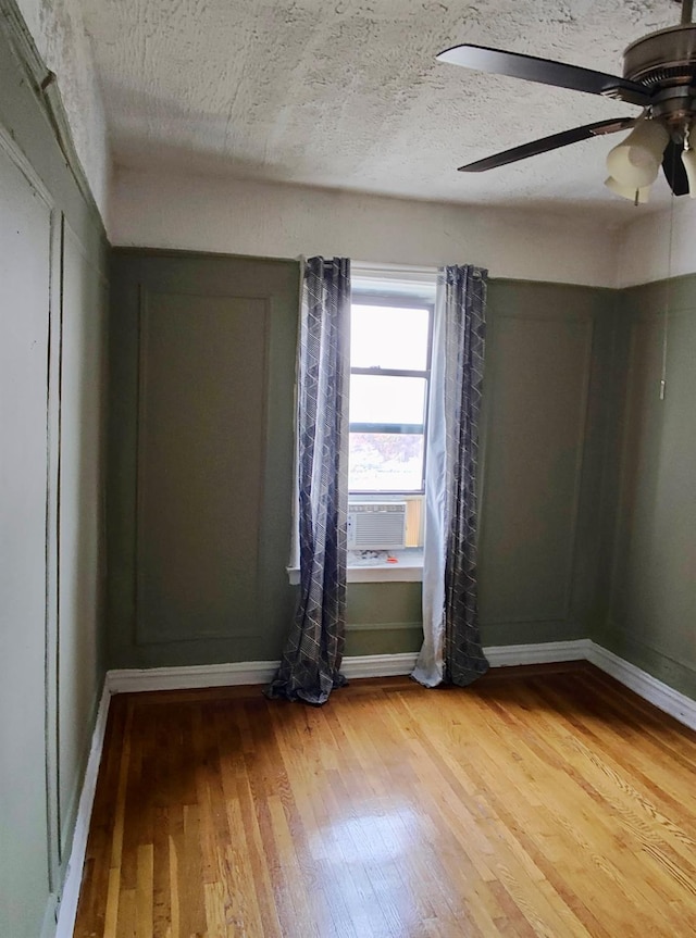 empty room with baseboards, light wood-style flooring, ceiling fan, a textured ceiling, and cooling unit