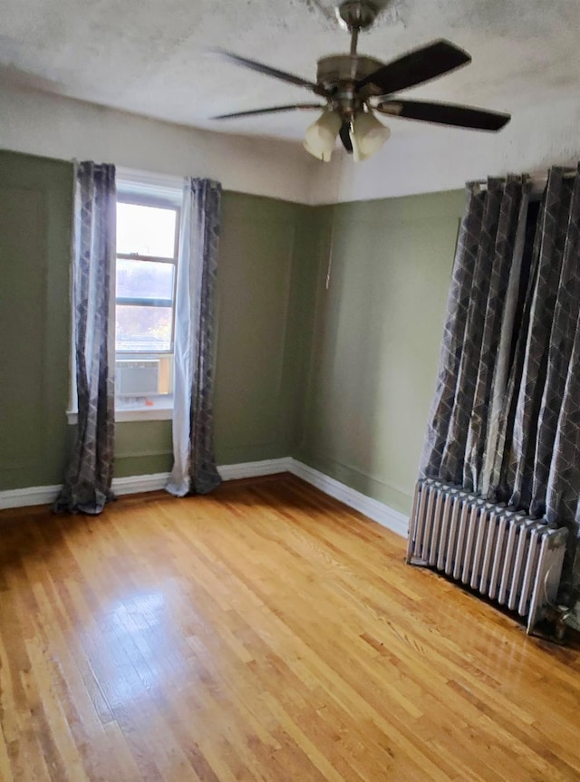 unfurnished room with baseboards, wood finished floors, a ceiling fan, and radiator