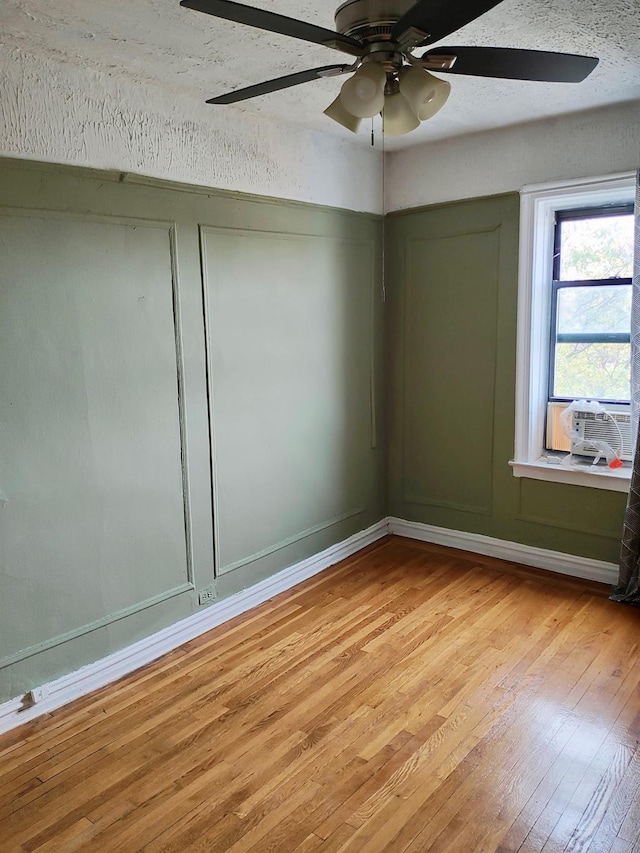 spare room with light wood-type flooring, cooling unit, ceiling fan, and baseboards