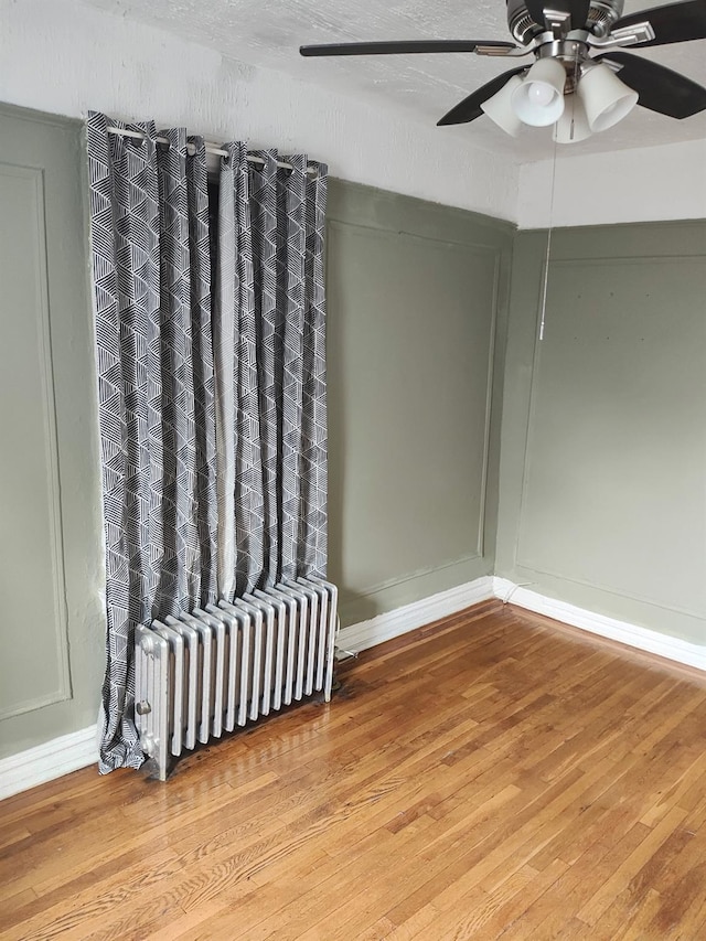 empty room with radiator heating unit, baseboards, ceiling fan, and wood finished floors