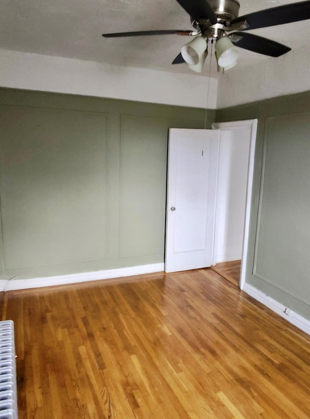 unfurnished room with radiator heating unit, a decorative wall, and wood finished floors