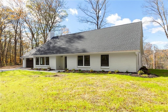 view of front of house with an attached garage, a shingled roof, a chimney, and a front yard