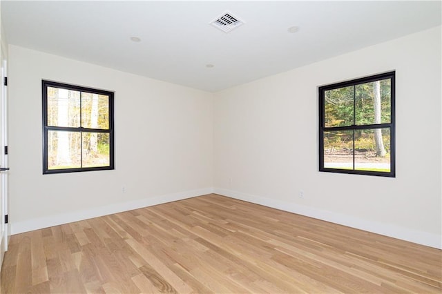 empty room featuring light wood-type flooring, visible vents, and baseboards