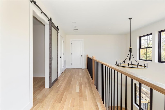 hallway with a notable chandelier, light wood finished floors, visible vents, a barn door, and baseboards