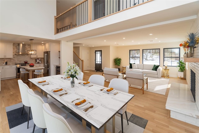 dining area with recessed lighting, a fireplace with raised hearth, stairway, and light wood finished floors