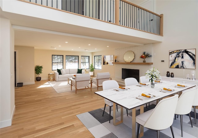 dining room with light wood finished floors, baseboards, a towering ceiling, a fireplace, and recessed lighting