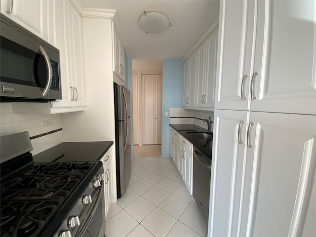 kitchen with light tile patterned floors, white cabinets, dark countertops, appliances with stainless steel finishes, and a sink