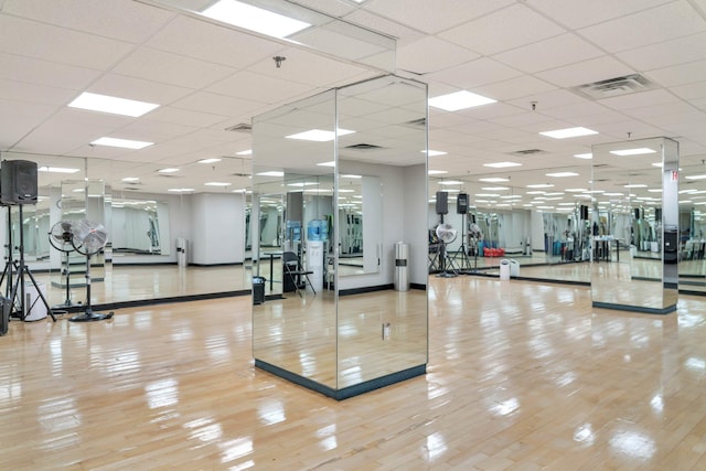 exercise room with light wood-type flooring, visible vents, and a paneled ceiling