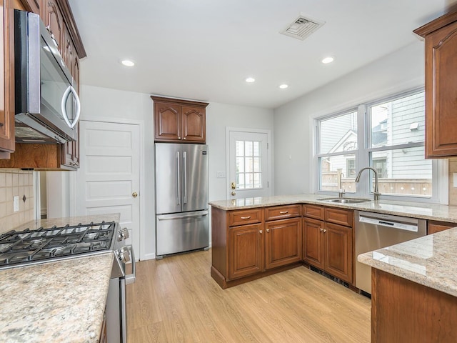 kitchen with light stone counters, stainless steel appliances, visible vents, a sink, and light wood-type flooring