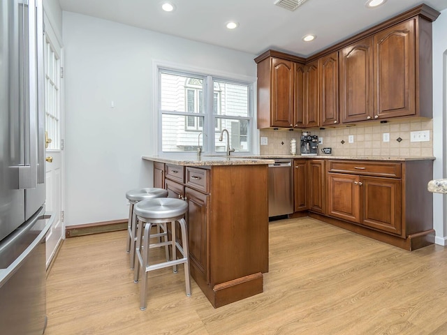 kitchen with light stone counters, a breakfast bar area, backsplash, light wood-style flooring, and appliances with stainless steel finishes