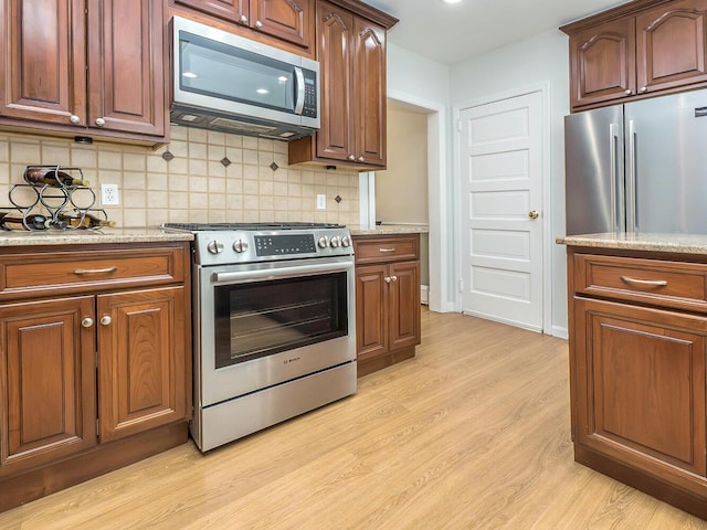 kitchen featuring appliances with stainless steel finishes, light wood-type flooring, light stone countertops, and tasteful backsplash