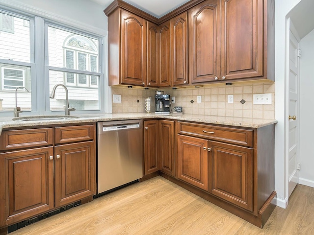 kitchen featuring a sink, stainless steel dishwasher, light wood-type flooring, light stone countertops, and tasteful backsplash