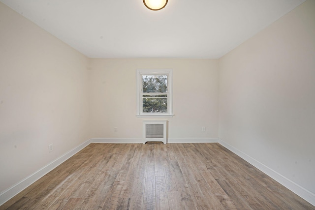 unfurnished room with radiator heating unit, wood finished floors, and baseboards