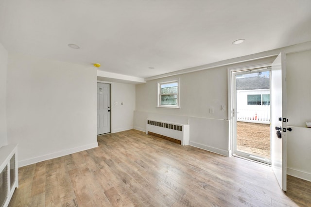 empty room featuring radiator heating unit, visible vents, baseboards, and light wood-style flooring