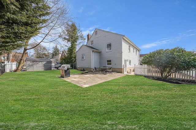 rear view of house with an outbuilding, a patio, a fenced backyard, a lawn, and a chimney